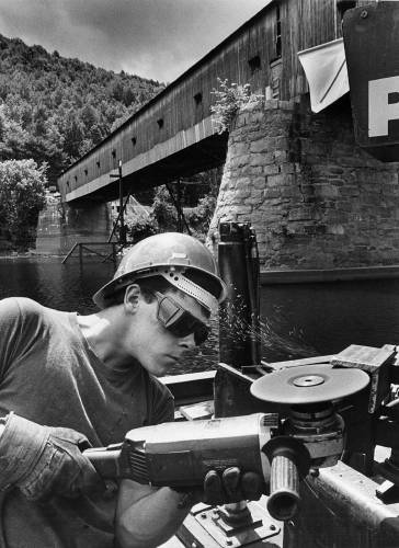 Keith Mulligan grinds a piece of iron to be welded onto an i-beam support during the reconstruction of the Cornish-Windsor Covered Bridge on July 1, 1988. (Valley News - Larry Crowe) Copyright Valley News. May not be reprinted or used online without permission. Send requests to permission@vnews.com.