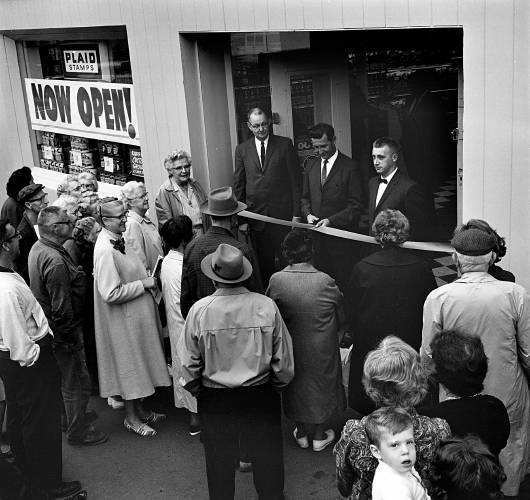 Bigger and better than ever is the description of the new A&P Supermarket in White River Junction, Vt., at its new location on the corner of Gates and South Main Street. On hand for the September 23, 1964, Grand Opening were A&P officials with Hartford Town Manager Ralph Lehman, shown center, cutting the ribbon. Minutes before the 9 a.m. opening, shoppers crowded the sidewalk to take advantage of the many sale specials and to get a first hand look at the store's up-to-date facilities. (Valley News - Larry McDonald) Copyright Valley News. May not be reprinted or used online without permission. Send requests to permission@vnews.com.