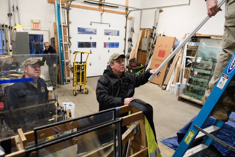 Claremont Glassworks employees Corey Oxland, right, hands parts for a retractable screen to Roger Rumrill, middle, while loading vans for the day's jobs with Shawn Eitapence, back left, and Matt Steele, left, in Claremont, N.H., on Thursday, Dec. 28, 2023. In April, Steele and his broghter Jonas took over the business, started in the late 1990s by their dad Keith Raymond. (Valley News - James M. Patterson) Copyright Valley News. May not be reprinted or used online without permission. Send requests to permission@vnews.com.