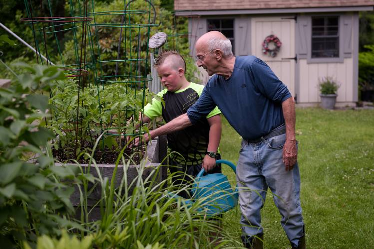 Al Pristaw, right, shows his neighbor Hunter Putnam, 9, how to check for moisture in the soil before watering at a raised bed in his yard at Riverside Mobile Home Park in Woodstock, Vt., on Tuesday, June 21, 2022. 