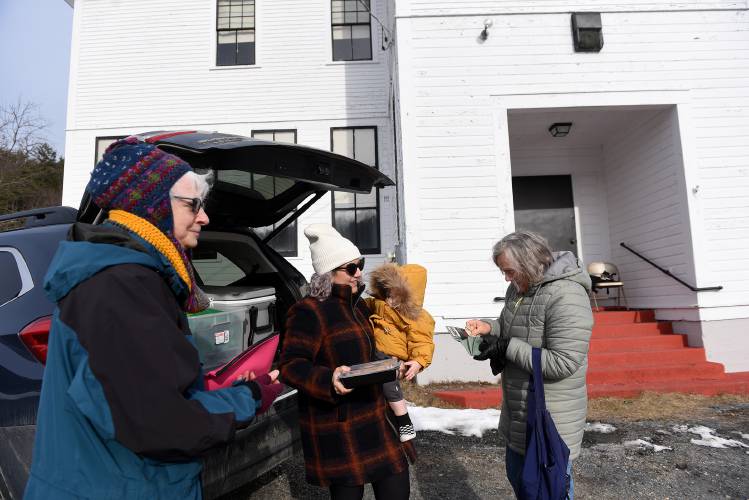 Kendall Gendron, of Corinth, Vt., holds her son Gilbert, 17 months, while handing Carole Freeman, of East Corinth, Vt., a chicken teriyaki dinner outside Gendron's non-profit building Miss Shannon's Schoolhouse on Friday, March 30, 2024. Rev. KellyAnn Donahue is on the left. The take-out dinners are being sold as a fundraiser for the East Corinth Congregational Church. (Valley News - Jennifer Hauck) Copyright Valley News. May not be reprinted or used online without permission. Send requests to permission@vnews.com.