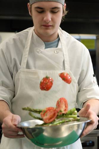 Nick Caver, 17, tosses asparagus and Roma tomatoes with olive oil, parsley and garlic during a practice session at Hartford Area Career and Technology Center in White River Junction, Vt., on Friday, March 1, 2024, for Junior Iron Chef Vermont. The competition challenges teams to use locally sourced ingredients to make simple, economical and nutritional meals. (Valley News - James M. Patterson) Copyright Valley News. May not be reprinted or used online without permission. Send requests to permission@vnews.com.