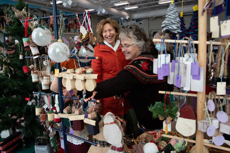 Pam Geason, left, of Etna, N.H., laughs as Cheryl Fogwill, of Newbury, N.H., shows her a variety of ornaments that she and her daughter Stacy Fogwill make and sell during an annual regional craft fair at Mascoma Valley Regional High School and Indian River Middle School in Canaan, N.H., on Saturday, Nov. 26, 2022. The Fogwills have been selling their Christmas decorations at the craft fair for over a decade and frequently see repeat customers. (Valley News / Report For America - Alex Driehaus) Copyright Valley News. May not be reprinted or used online without permission. Send requests to permission@vnews.com.