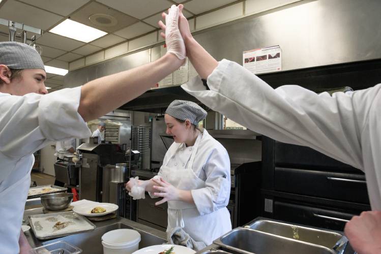 Jillianne Ballou, 17, middle, removes her gloves as Nick Caver, 17, left, and Reghan Allen, 17, right, celebrate after completing their recipe during a practice session for Junior Iron Chef Vermont at Hartford Area Career and Technology Center in White River Junction, on Friday, March 1, 2024. During competition, students assemble  all of their ingredients in 