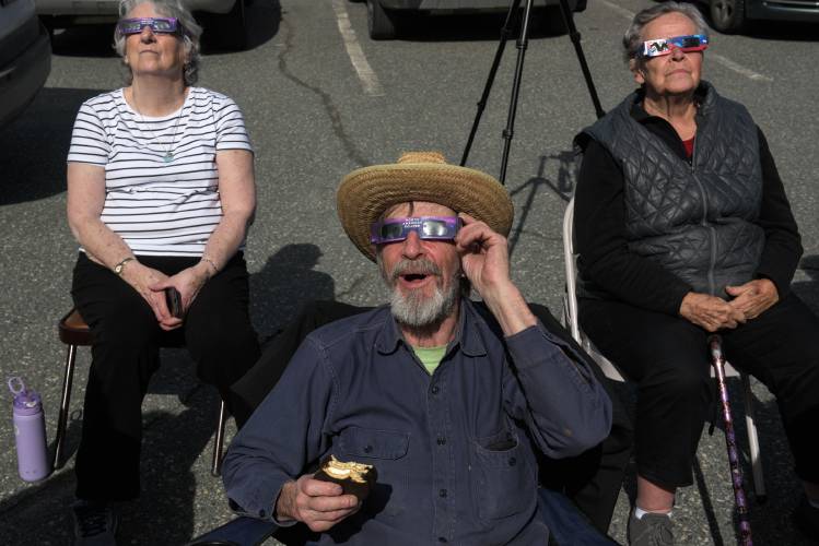 Don Mason, of White River Junction, middle, eats a moon pie while watching the solar eclipse with Carol Tucker, of West Lebanon, left, and Betty Ann Heistad, of Lebanon, right, during an eclipse watch party at the Bugbee Senior Center in White River Junction, Vt., on Monday, April 8, 2024. (Valley News - James M. Patterson) Copyright Valley News. May not be reprinted or used online without permission. Send requests to permission@vnews.com.
