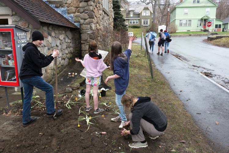 Chelsea Martin, 9, second from left, and Morgan Rothbart, 11, third from left, wave to students walking home from Newport Middle High School as they work on planting a bed of flowers with Micah Studios intern Justin Lord, left, and guide Stacey Hammerlind, right, outside Epiphany Episcopal Church in Newport, N.H., on Monday, April 18, 2024. (Valley News - James M. Patterson) Copyright Valley News. May not be reprinted or used online without permission. Send requests to permission@vnews.com.