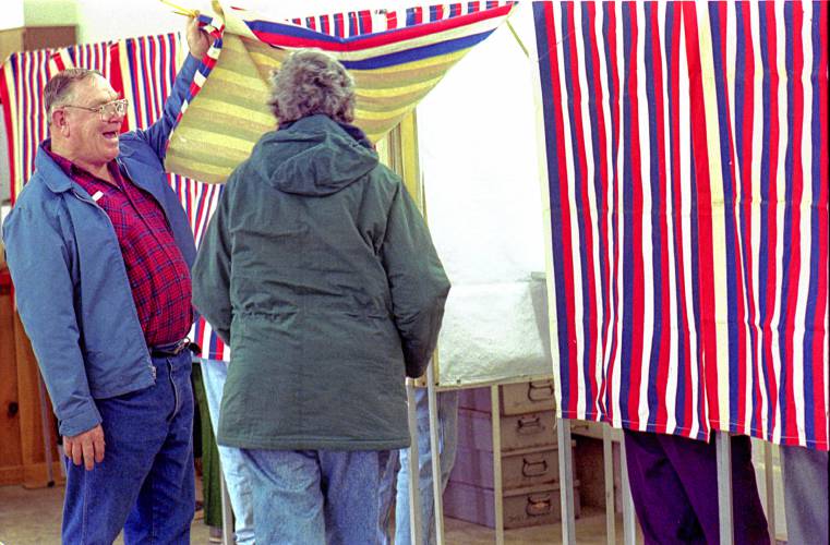 Canaan Selectboard member Tom Ireton lifts a voting booth curtain on April 8, 1997, during polling at the fire station in Canaan, N.H. It was the first year of ballot voting under New Hampshire's official ballot law, with a deliberative session to hear and amend the warrant on one day and voting by Australian ballot on another. A proposal to rescind the prior year's approval of law was defeated 434-365. (Valley News - Geoff Hansen) Copyright Valley News. May not be reprinted or used online without permission. Send requests to permission@vnews.com.
