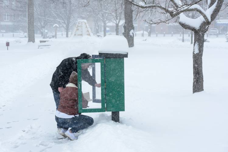 Josh Bellinger, standing, and Tasha Crockwell, crouching, browse the books in the Little Free Library at Colburn Park in Lebanon, N.H., on Saturday, March 23, 2023. They are both currently living nearby at Headrest and went out for a walk in the snow. 