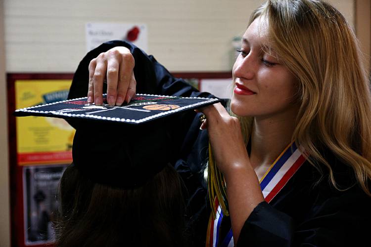 Ella Perreault, of Chelsea, Vt., kneels as White River Valley High School classmate Shannon Hadlock, of Montpelier, Vt., adjusts her mortarboard tassel as they get ready for their commencement ceremony in South Royalton, Vt., on June 17, 2023. (Valley News - Geoff Hansen) Copyright Valley News. May not be reprinted or used online without permission. Send requests to permission@vnews.com.