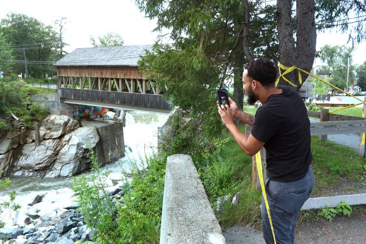 Devon Santos talks to his wife on the phone while checking out the Quechee covered bridge and dam on Wednesday, July 19, 2023, in Quechee, Vt. Santos, who lives in Cape Cod, is an electrician who has work at DHMC and had been swimming on July 6 at the bridge. Santos saw a social media post about the damage to the bridge and dam in Quechee and wanted to see what it looked like for himself. (Valley News - Jennifer Hauck) Copyright Valley News. May not be reprinted or used online without permission. Send requests to permission@vnews.com.