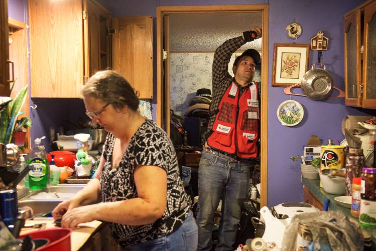 Red Cross Volunteer Al Hermsen, of Brookfield, installs a new smoke detector and Gwen LaCount washes dishes at left in the mobile home where her parents and brother live in West Newbury, Vt., on Saturday, Oct. 21, 2023. Gwen LaCount and her two adult children have been staying in the trailer since their adjacent mobile home was destroyed in a fire last July and are having difficulty finding new housing. (Valley News - James M. Patterson) Copyright Valley News. May not be reprinted or used online without permission. Send requests to permission@vnews.com.