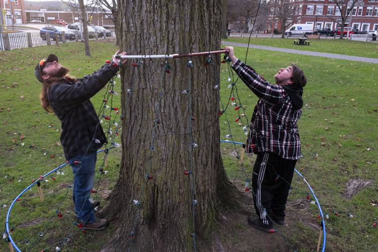 Devon Blanchard, 21, of West Fairlee, right, and his friend Carter Shannon, of Canaan, left, wait for Lebanon Recreation, Arts and Parks Director Paul Coats, not pictured, to secure a support for strings of holiday lights from a lift truck while setting up a display at Colburn Park in Lebanon, N.H., on Tuesday, Nov. 21, 2023. It is Blanchard's sixth year setting up a light display to honor his uncle Jason Timmons, who died tragically with his fiancée when their vehicle was struck on Interstate 89 by a pickup truck whose driver intentionally drove across the median in 2013. Blanchard's decorations will be part of the city's Downtown Winter Celebration this year and will be lit at 5:15 p.m. on Dec. 2. (Valley News - James M. Patterson) Copyright Valley News. May not be reprinted or used online without permission. Send requests to permission@vnews.com.
