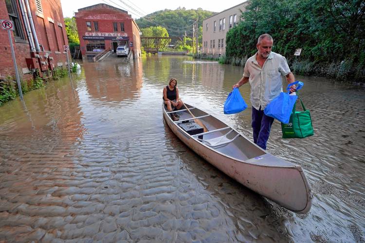 FILE - Jodi Kelly, seated center, practice manager at Stonecliff Veterinary Surgical Center, behind, and her husband Veterinarian Dan Kelly, right, use a canoe to remove surgical supplies from the flood damaged center, July 11, 2023, in Montpelier, Vt. The supplies included orthopedic implants for an upcoming surgery on a dog. (AP Photo/Steven Senne, File)