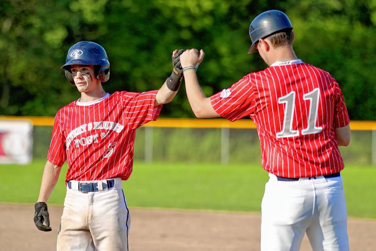 White River Junction Post 84 runner Drew Martin, left, high-fives first-base coach Colin Vielleux after reaching base during an American Legion senior baseball exhibition game on July 19, 2023, at the Maxfield Athletic Complex in White River Junction, Vt. Post 22 won, 10-9. (Valley News - Tris Wykes) Copyright Valley News. May not be reprinted or used online without permission. Send requests to permission@vnews.com.