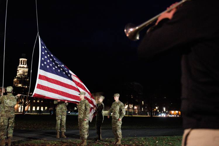 Dartmouth Army ROTC cadets, from left, Brian Zheng, Lintaro Donovan, Elias Moyse, Helen Connor, Cooper Hyldahl, obscured, Janelle Annor, obscured, Anne-Sarah Nichitiu, and Nathaniel Attia, lower the American Flag as Dartmouth freshman Jacob Crawford, right, plays 