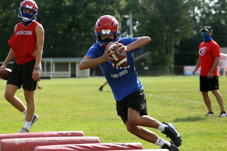 Hartford's Brayden Trombly runs through a footwork drill with other quarterbacks at the first practice for  7-on-7 football in White River Junction, Vt., on Sept. 8, 2020 as coach Matt Trombly watches. At left is returning starter Cole Jasmin. (Valley News - Geoff Hansen) Copyright Valley News. May not be reprinted or used online without permission. Send requests to permission@vnews.com.