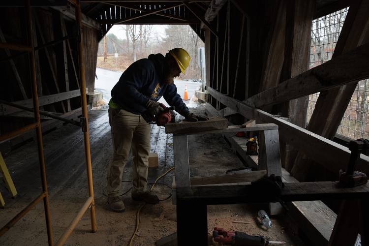 Lee Elwood of Daniels Construction cuts out wedges that will help secure newly replaced support beams at the Union Village Bridge in Thetford, Vt., on Wednesday, Jan. 18, 2023. The cost to repair the bridge, which was damaged in August, was approximately $12,845, most of which will be covered by insurance. Before the Daniels crew started repairing the months-old damage, the bridge was damaged again on Thursday, resulting in another $8,565 of pending repairs, according to Thetford Town Manager Bryan Gazda. “Our insurance company loves us,” he joked. (Valley News / Report For America - Alex Driehaus) Copyright Valley News. May not be reprinted or used online without permission. Send requests to permission@vnews.com.