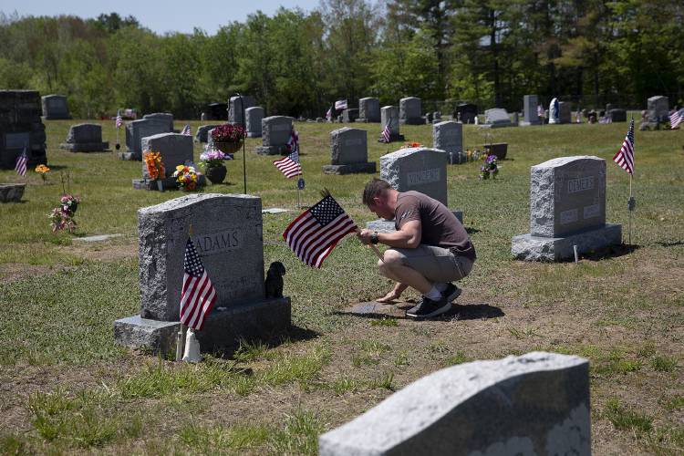 U.S. Marine Jeremy Williams, of Springfield, Vt., clears dirt from a grave marker while placing American flags by the headstones of veterans at Sacred Heart and Valley cemeteries in Lebanon, N.H., on Friday, May 26, 2023. Williams and several other veterans who work at Hypertherm placed flags ahead of Memorial Day on behalf of American Legion Post 22 in Lebanon, which places around 1,000 flags throughout the Upper Valley each year. (Valley News / Report For America - Alex Driehaus) Copyright Valley News. May not be reprinted or used online without permission. Send requests to permission@vnews.com.
