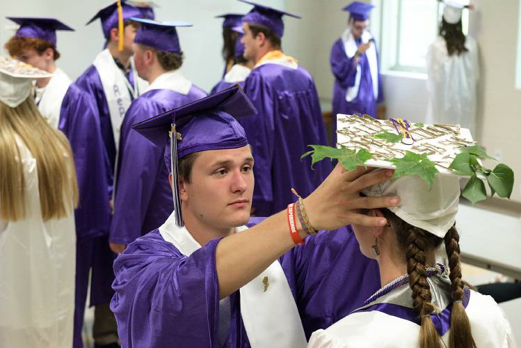 Logan Gilmore, left, straightens the cap of Alanna Cilbrith before Mascoma High School commencement in West Canaan, N.H., on Friday, June 16, 2023. Cilbrith decorated her mortarboard with a shell casing hat clip because she's a hunter, maple and lilac leaves and wore chainsaw tooth earrings for her plans of studying forestry. 