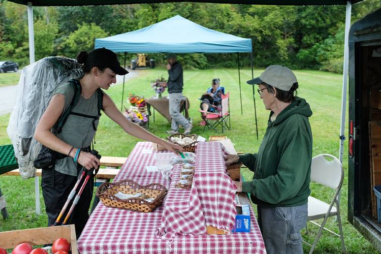 Appalachian Trail hiker Laura Dzubay, left, stops to buy cookies from Alice Lamson, of Fox Crossing Farm, at the West Hartford Library Farmers Market on her way through the Vermont village on Tuesday, Sept. 13, 2022. The market is in its last two weeks for the season, ending on Sept. 27. Martha and Zach Bryan, of Wilder Flowers, are in the background. (Valley News - James M. Patterson) Copyright Valley News. May not be reprinted or used online without permission. Send requests to permission@vnews.com.