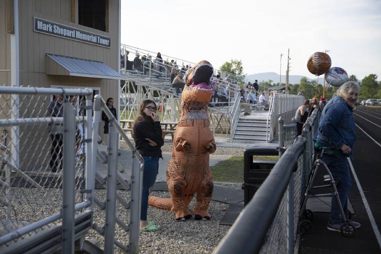 Newport sophomore Mallory Cornish, left, stands next to freshman Chloe Greenwood , clad in a blow-up Tyrannosaurus rex costume as they wait for graduates to process in at Newport High School in Newport, N.H., on Thursday, June 15, 2023. Greenwood’s cousin was graduating and she said the costume is a kind of tradition for him. (Valley News / Report For America - Alex Driehaus) Copyright Valley News. May not be reprinted or used online without permission. Send requests to permission@vnews.com.