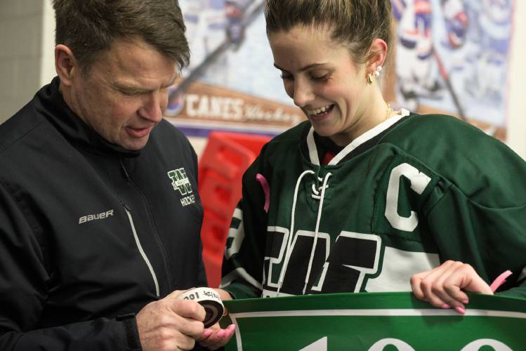 Ian Coates, head coach of Woodstock girls hockey, left, presents Gracelyn Laperle, right, with the puck from her 100th point scored during a 3-2 overtime win over Hartford at Barwood Arena in White River Junction, Vt., on Wednesday, Jan. 18, 2024. Laperle contributed two goals to the win. (Valley News - James M. Patterson) Copyright Valley News. May not be reprinted or used online without permission. Send requests to permission@vnews.com.