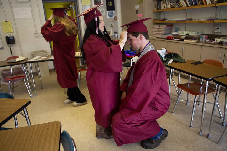 Montana Hanchett, right, crouches so Natalie Cutting can help him adjust his mortar board before their graduation ceremony at Hanover High School in Hanover, N.H., on Friday, June 9, 2023. (Valley News / Report For America - Alex Driehaus) Copyright Valley News. May not be reprinted or used online without permission. Send requests to permission@vnews.com.