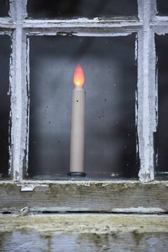 An electric candle glows in a Canaan Meetinghouse window in need of paint and re-glazing in Canaan, N.H., on Friday, Dec. 29, 2023. (Valley News - James M. Patterson) Copyright Valley News. May not be reprinted or used online without permission. Send requests to permission@vnews.com.