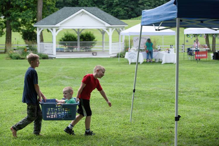 Ben Canterbury, 10, left, of Orford, and his cousin Wyat Reed, 8, right, carry Reed's brother Reuben, 2, a ride in a basket at the Orford (N.H.) Open Air Market on Saturday, July 22, 2023. Canterbury was selling antique bottles found with the help of his grandfather Tim Chase in an old farm dump, and Chase was selling his novel Castle Valley. (Valley News - James M. Patterson) Copyright Valley News. May not be reprinted or used online without permission. Send requests to permission@vnews.com.