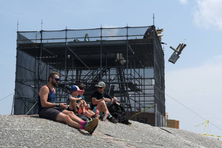 Hikers, from left, Matt Skoby, his son Carter, 6, Weston Beaulieu, 7, and his dad Tim Beaulieu, all of Concord, rest at the summit of Mount Cardigan after ascending the Holt Trail, as workers remove debris from the demolition of the mountain’s fire tower in Orange, N.H., on Thursday, August 10, 2023. (Valley News - James M. Patterson) Copyright Valley News. May not be reprinted or used online without permission. Send requests to permission@vnews.com.