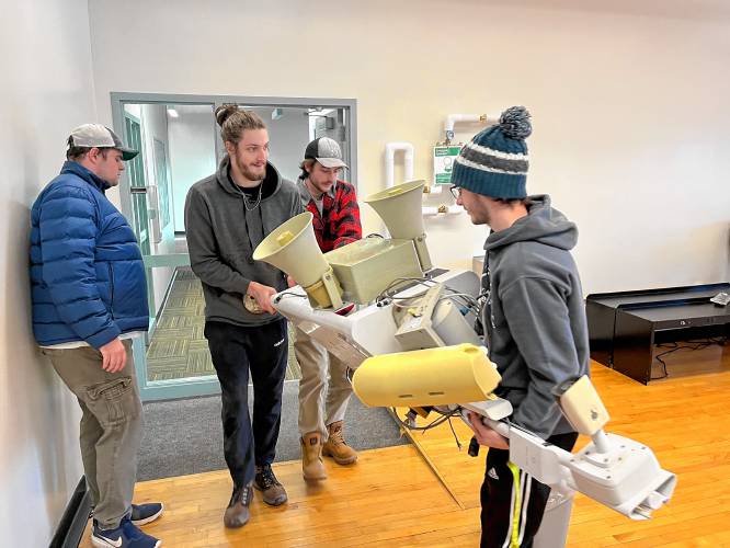 Robotics program students at Plymouth State University carrying a scarecrow robot on loan from Casella into the robotics lab in the Draper & Maynard building in spring 2023. The team is rehabilitating two of the robots, which scare away animals and birds from landfills.