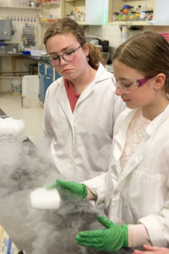 Aila Butler, 15, of Lyme, left, and Maddy Amell, of Norwich, right, play with dry ice, the solid state of carbon dioxide, frozen at negative 78 degrees celsius, in the lab at New Hampshire Academy of Science in Lyme, N.H., Thursday, April 11, 2024. When pushed across the table, the block floats on a layer of carbon dioxide gas formed when the solid sublimates or turns directly from its solid state to gas. “Science is a good way to understand the world around us,” said Butler. “Whether that be the natural world or society.” (Valley News - James M. Patterson) Copyright Valley News. May not be reprinted or used online without permission. Send requests to permission@vnews.com.