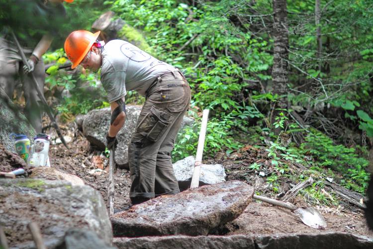 Emily White, the crew lead for the restoration project of the Old Bridle Path, moves a rock to create a staircase up the trail. 