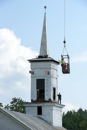 Jan Lewandoski, of Stannard, stands below waiting to receive a lengths of trim Mike Cotroneo, of Morrisville, and Adam King, of Roxbury, in the basket of a crane, are removing from the steeple of the First Universalist Church and Society of Barnard in preparation to remove the spire in Barnard, Vt., on Wednesday, July 19, 2023. “Imagine when you have a thing that’s 70 or 90 feet long and a powerful wind hits it, once every 30 years even,” said Lewandoski who is leading the restoration of the structure. “It’s a tremendous lever arm and it jams it backward. Almost all of them you’ll see lean back a little bit.” (Valley News - James M. Patterson) Copyright Valley News. May not be reprinted or used online without permission. Send requests to permission@vnews.com.
