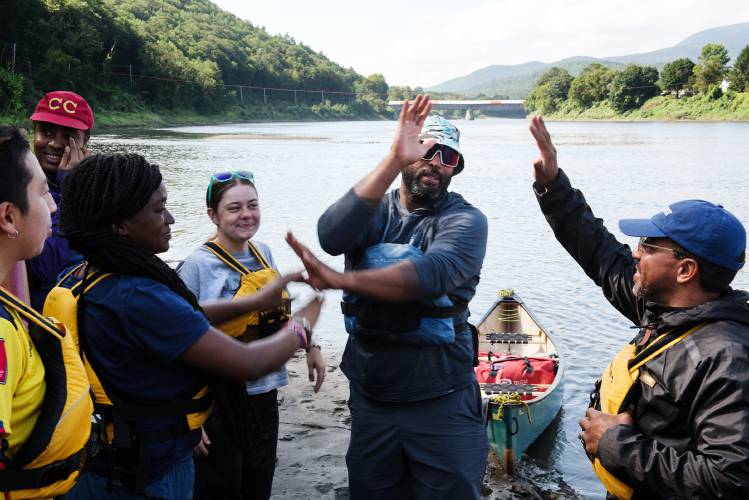 Rutgers University professor Clayton Walton, center right, congratulates students after completing their unguided paddle on the Connecticut River from Windsor, Vt., to Cornish, N.H., on Tuesday, August 29, 2023, the final day of their Sustainable Living Intensive. The culmination of a course on sustainable development, the group traveled from Newark, N.J. for four days at the Kroka Expeditions farm in Marlow, N.H., before a four day paddle as a way to engage with the natural world. “One of our highlights is seeing the stars at night time,” said Luis Torres, right, a recent Rutgers graduate. “We just don’t see that where we’re from.” From left are students Richardt Morocho, Shampa Sydney, Sarah Delva, Karolina Leleniewski, Walton, and Torres. (Valley News - James M. Patterson) Copyright Valley News. May not be reprinted or used online without permission. Send requests to permission@vnews.com.
