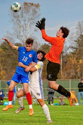 Milton High goalkeeper Dylan Mitchell leaps to catch the ball while teammate Tyler Larocque pulls on Hartford's Sam Peckinpaugh (10) during the Vermont Division II teams' first-round playoff game on Oct. 25, 2023, on White River Junction, Vt. Milton won, 2-1, in overtime. (Valley News - Tris Wykes) Copyright Valley News. May not be reprinted or used online without permission. Send requests to permission@vnews.com.
