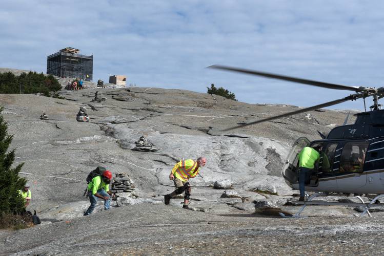 As a trio of hikers watches from above, Valley Restoration workers Craig Lawlor, left, and Christopher De La Rosa, second from left, Bob McGlothin, right, and Mark McAfee, of North American Helicopters, second from right, board the last flight off Mount Cardigan in Orange, N.H.,  mountain after assembling the roof and walls of the new fire tower cab on Friday, Oct. 27, 2023. After more than three months of contending with weather delays, the new cab structure is in place and finish work can begin.(Valley News - James M. Patterson) Copyright Valley News. May not be reprinted or used online without permission. Send requests to permission@vnews.com.