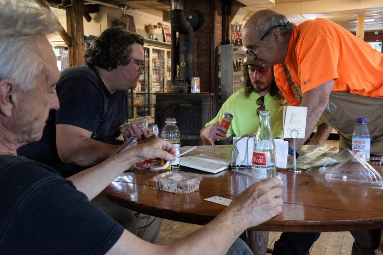 Adam King, of Roxbury, second from left, Joe Cotter, of Northfield, second from right, and Mike Cotroneo, of Morrisville, right, look over a map for an assessment project of King’s as Jan Lewandoski, of Stannard, left, relaxes during lunch at the Barnard General Store after taking down the spire of the First Universalist Church in Barnard, Vt., on Wednesday, July 19, 2023. “Thank God,” said Lewandoski when the spire was safely on the ground. (Valley News - James M. Patterson) Copyright Valley News. May not be reprinted or used online without permission. Send requests to permission@vnews.com.