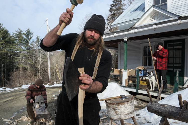 Will Lisak, of Royalton, middle, hammers home a wedge to complete a new handle for his broad ax as Nevan Carling, of Hartford, Conn., works on his own handle and Adam Adeane, of East Poultney, looks on with his dog Wiley at right, outside Lisak’s Royalton, Vt., home on Thursday, Feb. 22, 2024. “It kind of was a bet to see if I could make a handle in less than an hour,” said Lisak. The pair, who are interested in using pre-industrial building methods, wanted to re-hang their ax heads before going to hew a sill beam for a client. (Valley News - James M. Patterson) Copyright Valley News. May not be reprinted or used online without permission. Send requests to permission@vnews.com.
