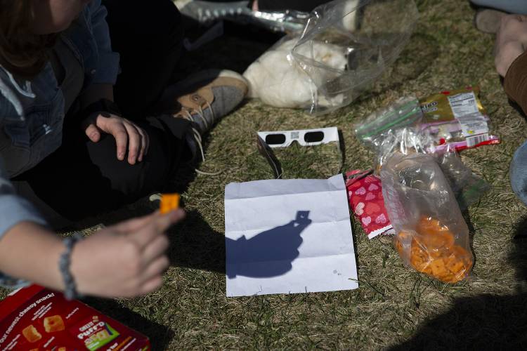 Erica Holmes, of Norwich, Vt., casts a a crescent of light through a Cheez-It during a total solar eclipse while sitting with her twin, Stephanie, and their Hanover High School classmate Noah Burdick, also of Norwich, in St. Johnsbury, Vt., on Monday, April 8, 2024. The twins lived in Colorado during the eclipse in 2017 and wanted to witness totality for the first time. “It’s 100% or nothing,” Burdick said. (Valley News / Report For America - Alex Driehaus) Copyright Valley News. May not be reprinted or used online without permission. Send requests to permission@vnews.com.