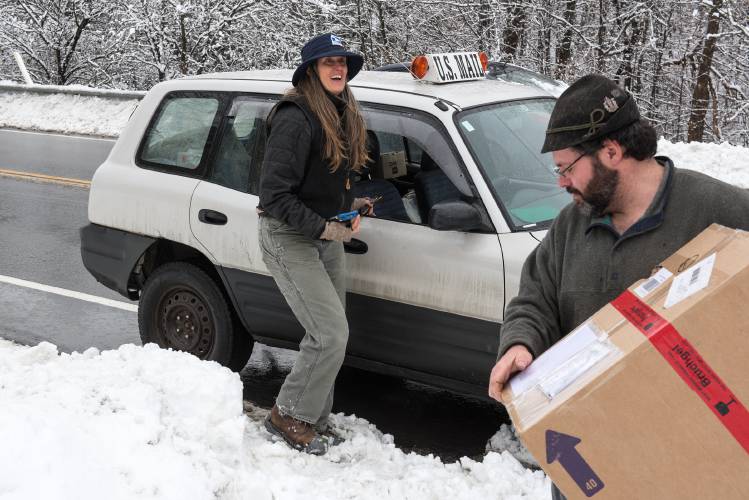 Mail Carrier Jennifer Brown, left, leaves a package with Maurizio Odermatt, right, at his home in Vershire, Vt., during a power outage on Monday, Dec. 4, 2023. Brown said that even though it's the busiest time of year, she enjoys working during the holidays because people are happy to see her when she brings their packages. (Valley News - James M. Patterson) Copyright Valley News. May not be reprinted or used online without permission. Send requests to permission@vnews.com.