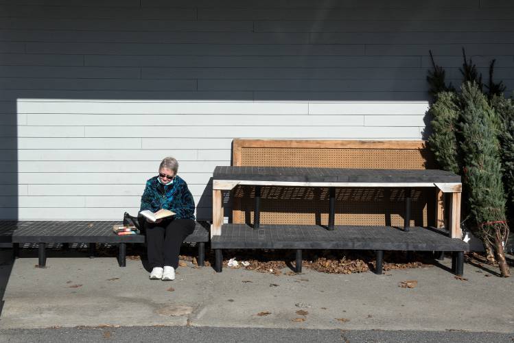 Liz Jones, of Londonderry, N.H., reads in a sunny, warm spot she found outside the Co-Op Food Store in White River Junction, Vt., while waiting for her daughter to finish a job interview on Monday, Nov. 20, 2023. She found the book at a take-one, leave-one shelf outside the building and was enjoying watching the grocery shopping rush in front of the store. (Valley News - James M. Patterson) Copyright Valley News. May not be reprinted or used online without permission. Send requests to permission@vnews.com.
