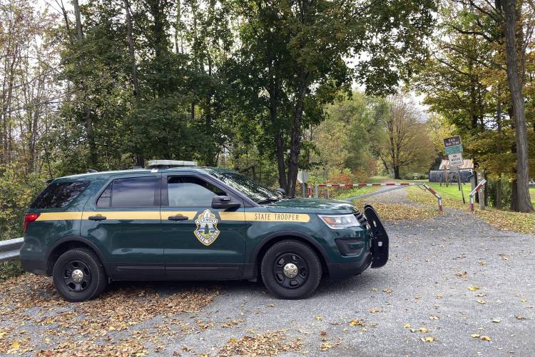 FILE - A Vermont State Police trooper sits parked in a cruiser on Oct. 11, 2023, at the entrance to a recreational trail in Castleton, Vt. Police are searching for the killer of a 77-year-old retired college dean who was shot while walking on the trail on Oct. 5. (AP Photo/Lisa Rathke, File)