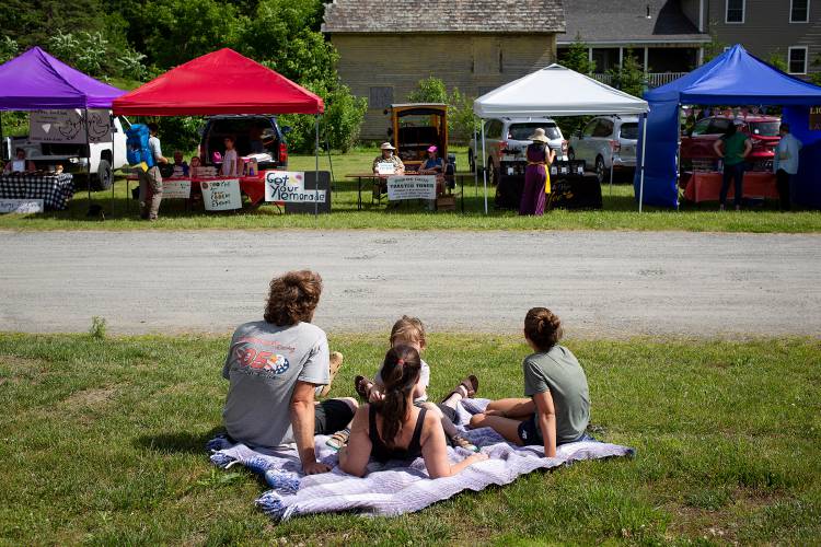 From left, Duncan Pogue, Katie Williams and Skye Pogue, 2, all of West Hartford, Vt., sit with Samana Sukumar during the first farmers market of the season at the West Hartford Public Library in West Hartford on Tuesday, June 14, 2022. The market has been on hiatus during the pandemic and this was the first time it was held since 2019. (Valley News / Report For America - Alex Driehaus) Copyright Valley News. May not be reprinted or used online without permission. Send requests to permission@vnews.com.