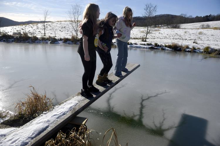 Friends Paige Smith, left, of East Corinth, Vt., Adi Maverick, of Corinth, Vt., and Harper Green, of East Corinth, balance on a diving board over a pond on Maverick's family's land on Saturday, Nov. 25, 2023. During the summer they swim in the pond, on this cold and sunny day they were checking the thickness of the ice by throwing rocks on the pond. All three girls are 10 and attend school together. (Valley News - Jennifer Hauck) Copyright Valley News. May not be reprinted or used online without permission. Send requests to permission@vnews.com.