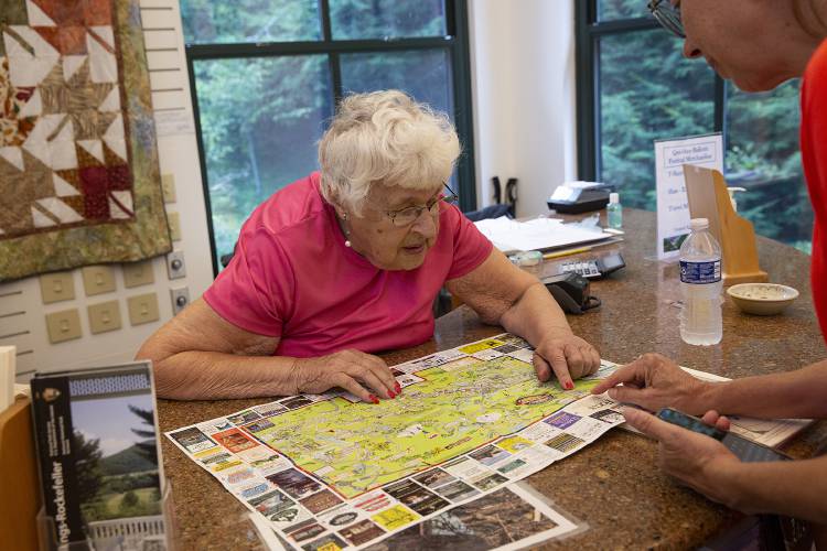 Charlotte Harvey, 91, left, of White River Junction, Vt., helps Martha Warmuth, of Nashville, Tenn., with directions to the President Calvin Coolidge State Historic Site in Plymouth, Vt., while working as a greeter at the Quechee Gorge Visitors Center in Quechee, Vt., on Tuesday, August 22, 2023. Harvey volunteers one day a week at the visitors center, where she has worked for over 20 years. “I really can’t imagine not working, but the time will come,” Harvey said. “I absolutely love it. I love every minute of it.” (Valley News / Report For America - Alex Driehaus) Copyright Valley News. May not be reprinted or used online without permission. Send requests to permission@vnews.com.