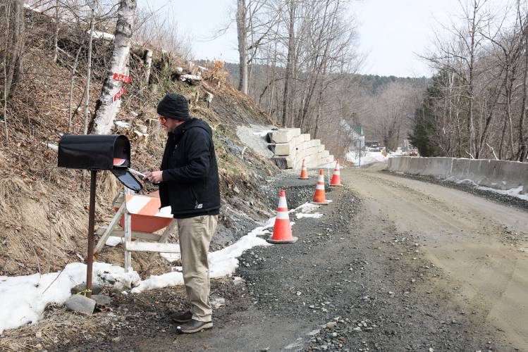 Evan Burnham checks the mail at the intersection of his driveway and Broad Brook Road in Royalton, Vt., on Thursday, Feb. 22, 2024. The road reopened to one lane of traffic on January 12, after being closed since July’s flooding caused landslides along the steep bank down to Broad Brook. 