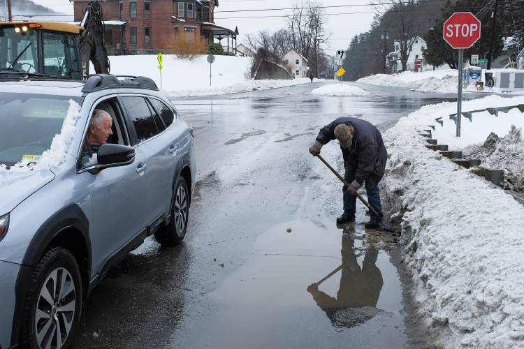 Stuart Dumville, of Royalton, calls out a greeting to Demi Boles, of the Royalton Highway Department, as he uncovers storm grates to drain water collecting on Chelsea Street in South Royalton, Vt., on Wednesday, Jan. 10, 2024, after a storm brought heavy snow followed by rain overnight. 