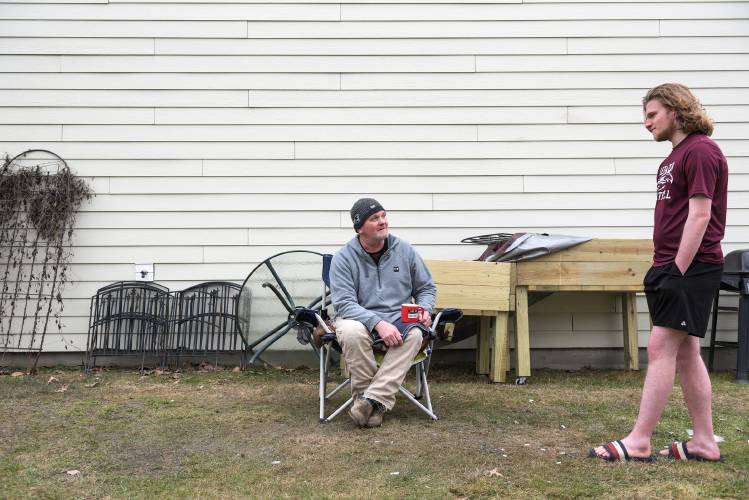 Conlyn Matson, 17, right, joined his dad Eric Matson, left, as he sat outside his Romano Circle apartment having coffee and a cigarette in West Lebanon, N.H., on Monday, Feb. 12, 2024. “I’m outside all winter,” said Matson a single dad of four kids. “It’s always been my escape.” Conlyn said he prefers warmer weather. (Valley News - James M. Patterson) Copyright Valley News. May not be reprinted or used online without permission. Send requests to permission@vnews.com.