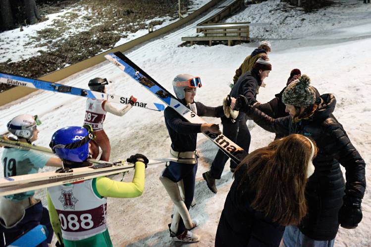Adam Goodney, center, gets a fist bump from Hanover alpine ski coach Gabi Formankova, right, as he climbs the hill with his Hanover ski jumping teammates after a meet at Oak Hill in Hanover, N.H., on Thursday, Feb. 1, 2024. Goodney placed seventh with 196 points. Hanover won the meet with 393.5 points. (Valley News - James M. Patterson) Copyright Valley News. May not be reprinted or used online without permission. Send requests to permission@vnews.com.
